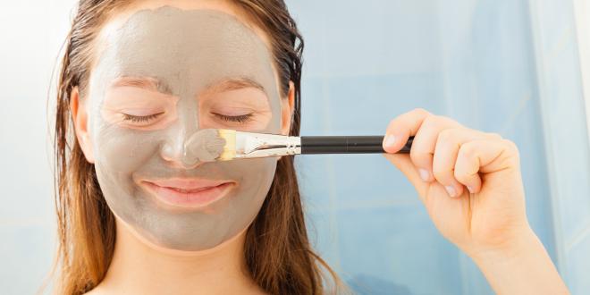 a teenage girl applying a gray mud facial mask