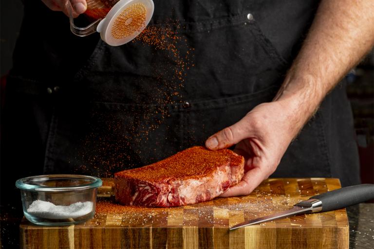 a man sprinkling dry rub on a strip steak